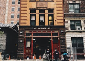 Classic fire station in urban setting with workers and construction cones on street.